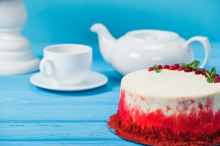 cake decorated with red currants and mint leaves between white cup, tea pot and stand isolated on blueの写真素材