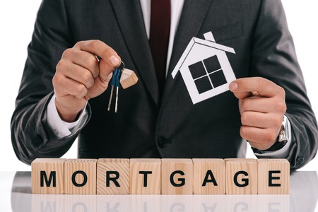 cropped view of mortgage broker holding paper house and keys near wooden blocks isolated on whiteの写真素材