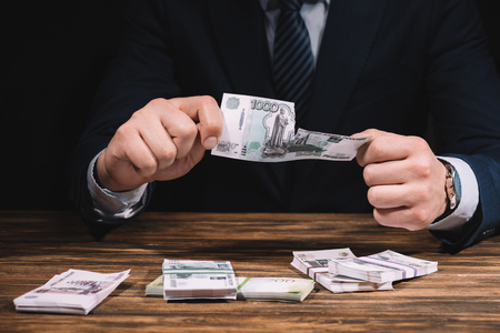 mid section of businessman ripping banknote above wooden table with russian rublesの写真素材