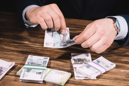 cropped shot of businessman ripping banknote above wooden table with russian rublesの写真素材