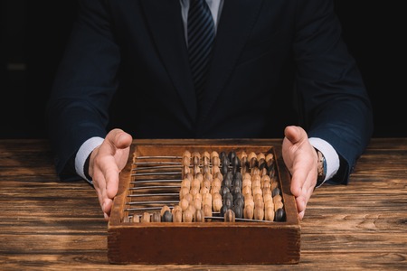 cropped shot of businessman holding counting frame while sitting at wooden table