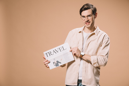 smiling man holding travel newspaper  isolated on beigeの写真素材