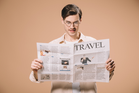 handsome man in glasses reading travel newspaper isolated on beigeの写真素材
