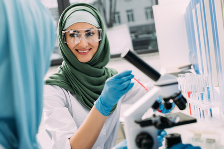 smiling female muslim scientist in goggles and hijab during experiment in chemical laboratoryの写真素材