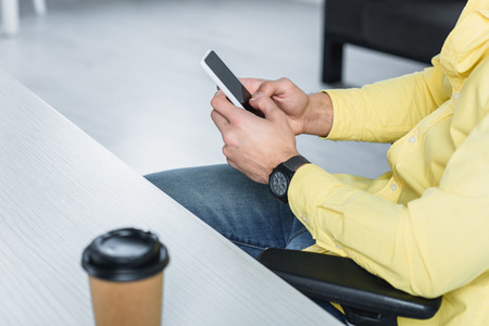 Partial view of man holding smartphone at workplace