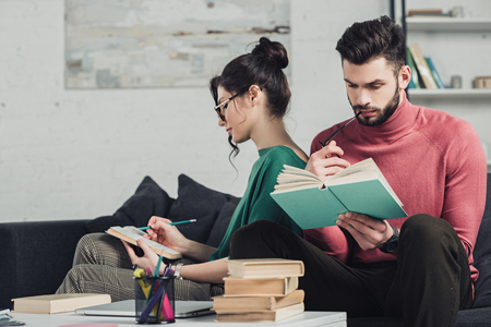 handsome man studying with book near girlfriend at homeの写真素材