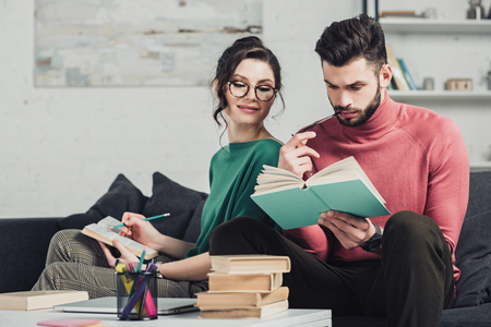 cheerful woman in glasses looking at boyfriend studying with bookの写真素材