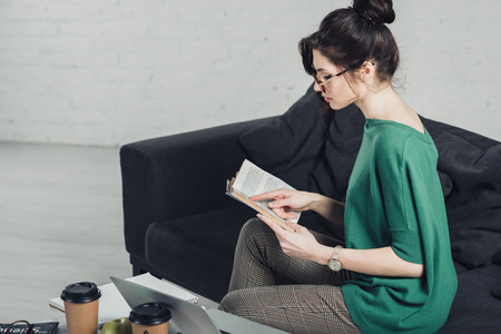 attractive woman studying with book and sitting on sofa