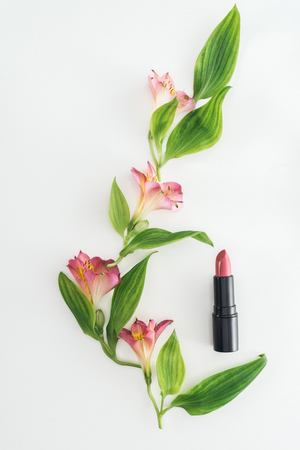 top view of composition with pink flowers, green leaves and lipstick on white backgroundの写真素材