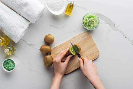 cropped view of woman cutting kiwi on wooden cutting desk on white surfaceの写真素材