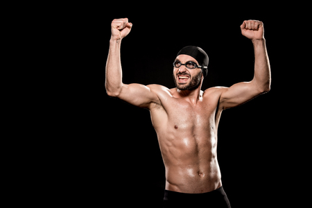 cheerful swimmer standing in swimming cap and celebrating victory isolated on blackの写真素材