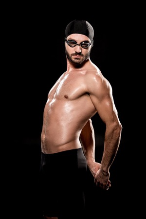 muscular swimmer posing in swimming cap and goggles isolated on blackの写真素材