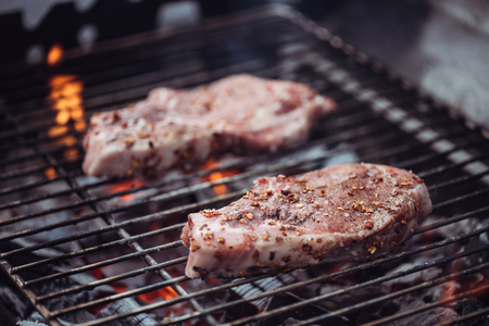 selective focus of juicy raw steaks grilling on barbecue gridの写真素材