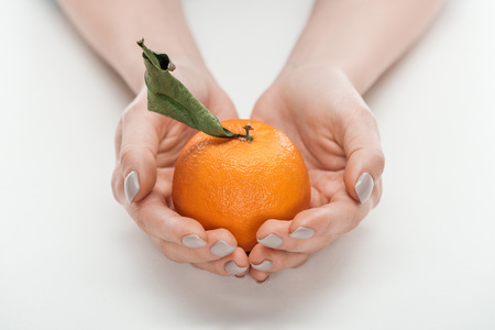 partial view of woman holding ripe whole unpeeled tangerine with leaf on white backgroundの写真素材