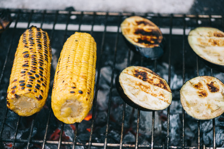 selective focus of yellow corn with crust and eggplant slices grilling on barbecue gridの写真素材
