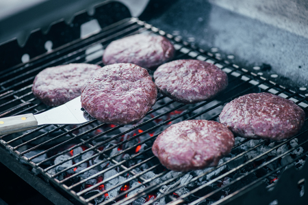 selective focus of spatula and uncooked fresh burger cutlets grilling on bbq gridの写真素材