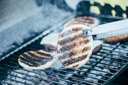 selective focus of tweezers and delicious fresh burgers ingredients with crust grilling on barbecue...