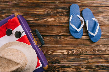 top view of summer accessories and flip flops near suitcase on wooden backgroundの写真素材