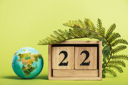 wooden calendar with date "22 april" and green fern leaf on light green backgroundの写真素材