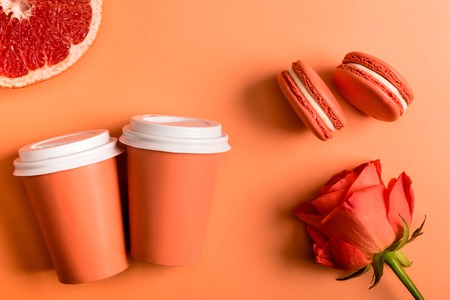 coral paper cups, rose flower, macarons and grapefruit half on coral background, color of 2019...