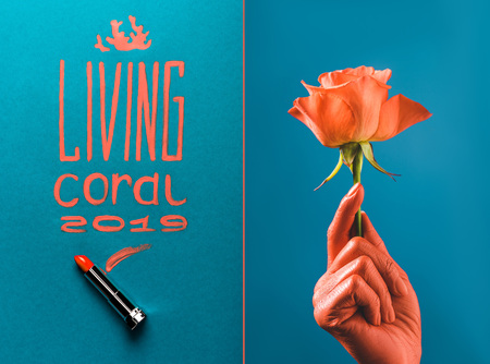 color of year 2019 handwritten lettering with coral lipstick, and partial view of coral colored female hand with coral rose on blue divided backgroundの写真素材