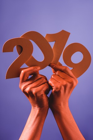 partial view of coral colored female hands with paper cut 2019 numbers on blue background, color of...