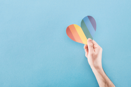 cropped view of male hand with rainbow colored paper heart on blue background, lgbt conceptの写真素材