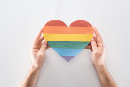 partial view of man holding paper rainbow colored paper heart on grey background, lgbt conceptの写真素材