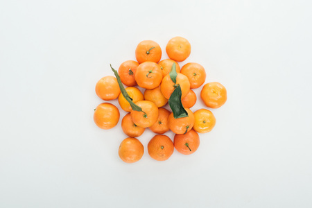 top view of bright ripe orange tangerines with green leaves stacked in pile on white backgroundの写真素材