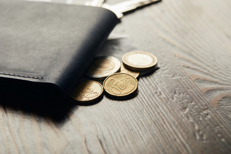 close up of leather wallet and coins on wooden table