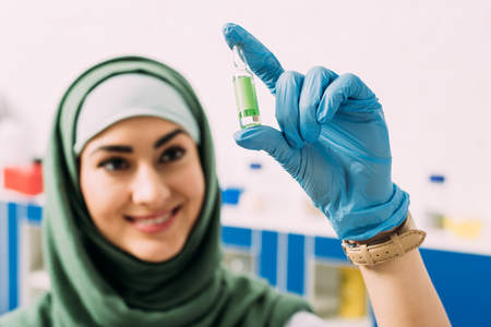 smiling female muslim scientist holding glass ampoule in laboratoryの写真素材