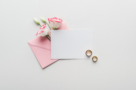 top view of empty card with pink envelope, flowers and golden wedding rings on grey backgroundの写真素材