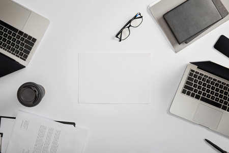 top view of documet on clipboard, paper cup, laptops, pen, notebooks, folder, glasses and blank paperの写真素材