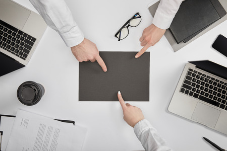 top view of businesspeople pointing to blank grey paper at workplace