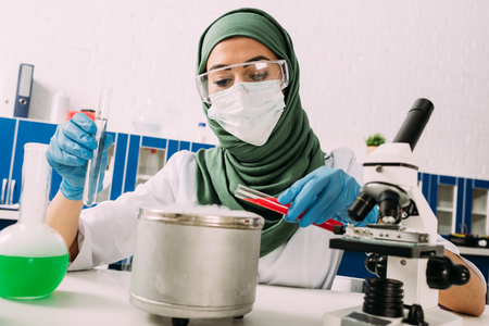 female muslim scientist holding test tubes over pot with dry ice during experiment in labの写真素材