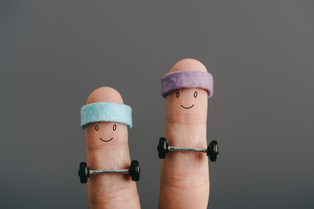 cropped view of smiling sporty fingers in headbands training with barbells isolated on grey