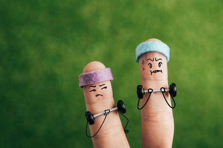 cropped view of sporty fingers in headbands training with barbells on green