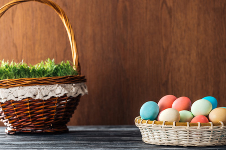 wicker basket with grass and bowl with easter eggs on wooden background