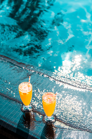 two glasses of orange juice with straws standing at poolsideの写真素材