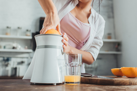 partial view of girl making fresh orange juice with juicer at wooden table in kitchenの写真素材