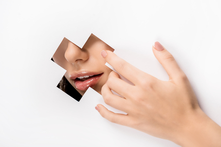 cropped shot of female hand and lips through cross shaped hole on whiteの写真素材