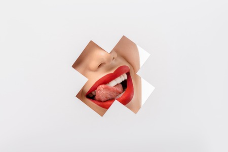 cropped shot of girl licking lips through cross shaped hole on whiteの写真素材