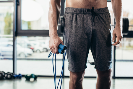 mid section of shirtless sportsman holding jumping rope in gymの写真素材