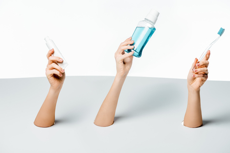 partial view of women holding toothpaste, toothbrush and mouthwash through holes on whiteの写真素材