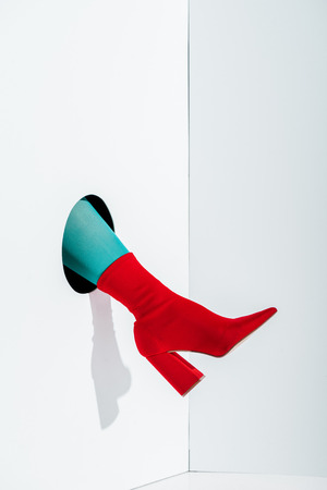 cropped image of girl showing leg in bright turquoise tights and red shoe in hole on whiteの写真素材