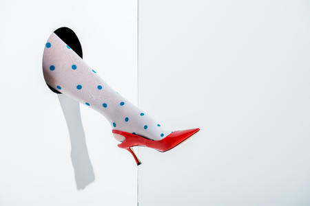 cropped image of woman showing leg in white tights with blue dots and red high heel in hole on whiteの写真素材