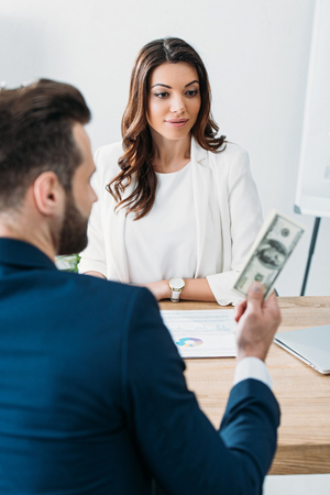 selective focus of advisor looking at investor holding dollar banknotesの写真素材