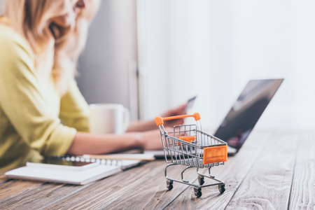 selective focus of small shopping trolley with woman using laptop on backgroundの写真素材