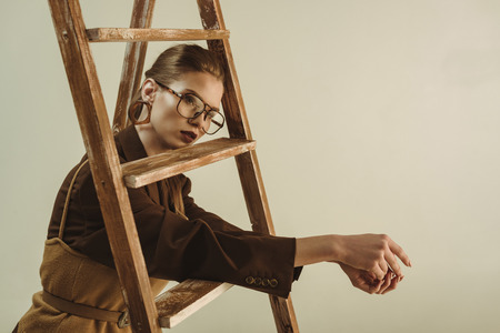 fashionable young woman in retro style posing near wooden ladder isolated on beigeの写真素材