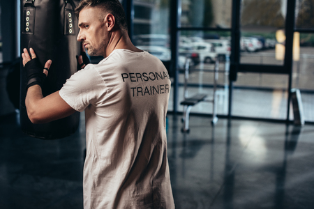 back view of personal trainer touching punching bag in gymの写真素材